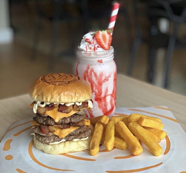 a hamburger and french fries on a plate with a strawberry milkshake in the background