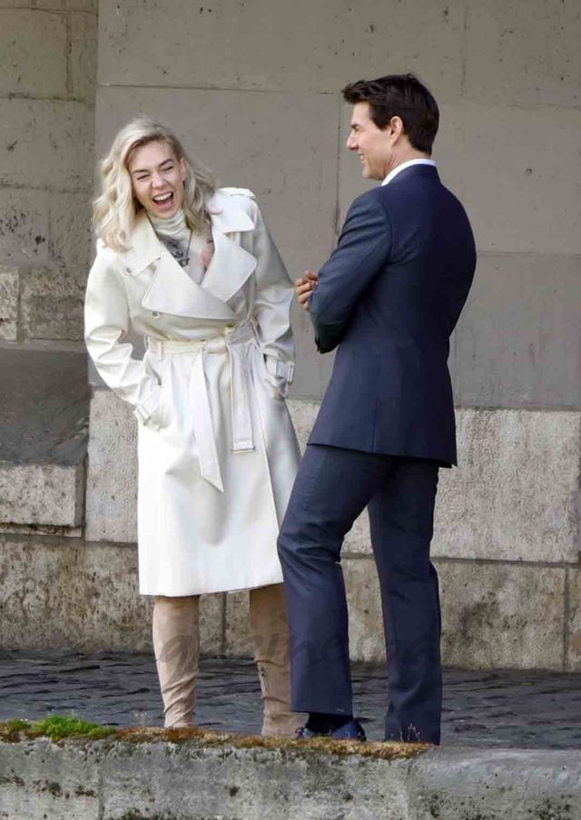 a man standing next to a woman in a white coat and tan boots on the street