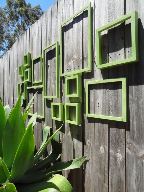 a wooden fence with green frames on the side and some plants in front of it