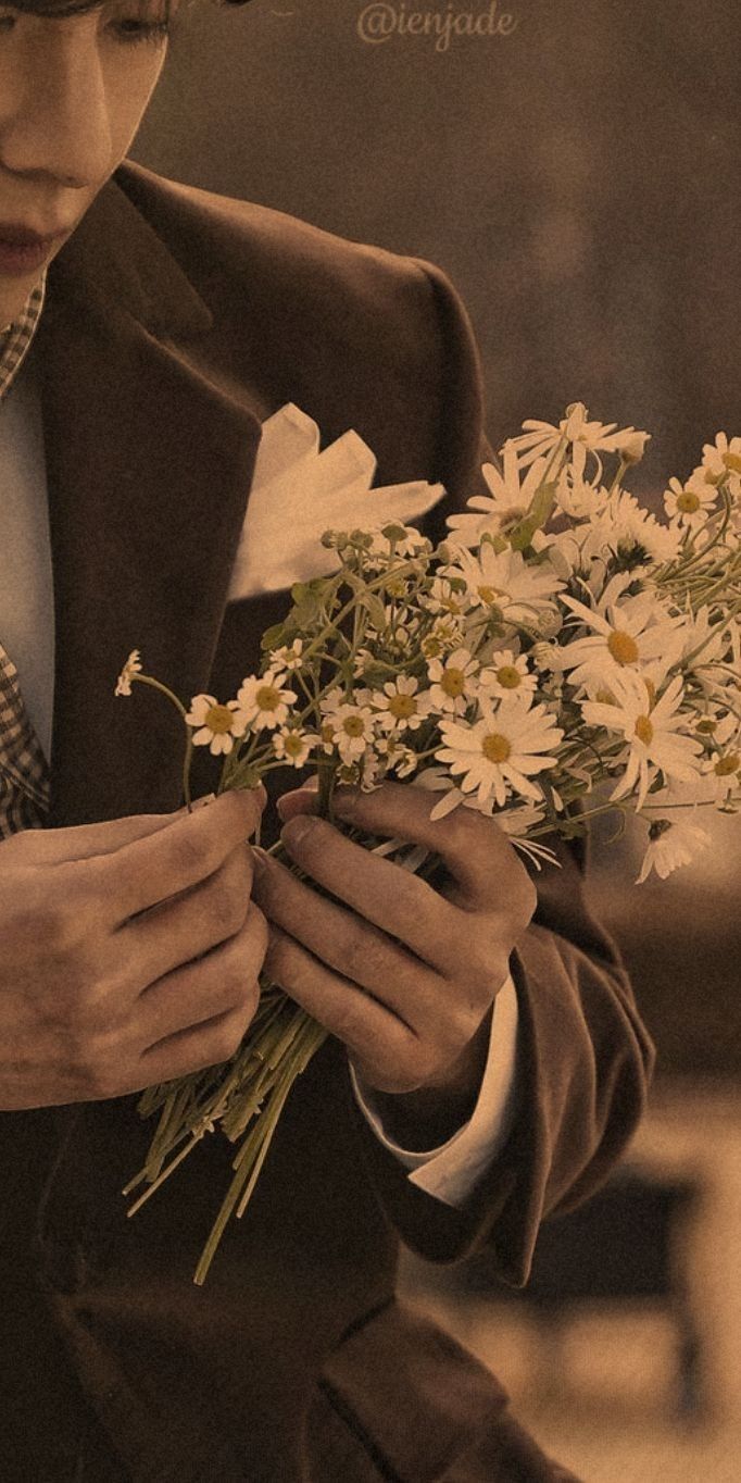 a man wearing a suit and tie holding a bouquet of daisies in his hands