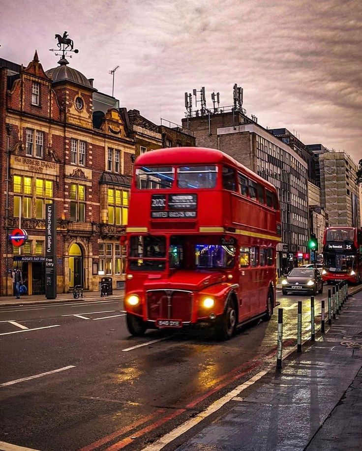 a red double decker bus driving down a street next to tall buildings and traffic lights