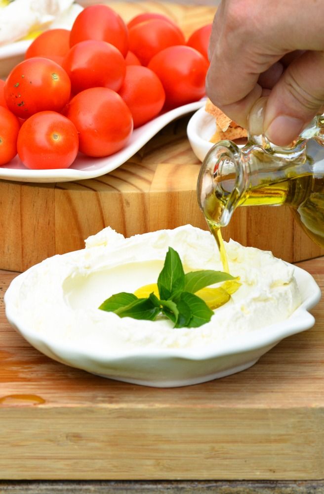 a person pouring olive oil onto a plate with tomatoes in the background