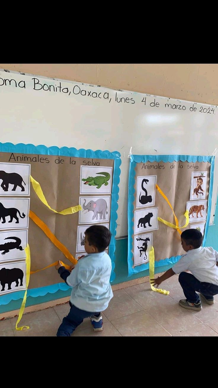 two children playing with paper animals in front of a bulletin board that has pictures of elephants and other animals on it