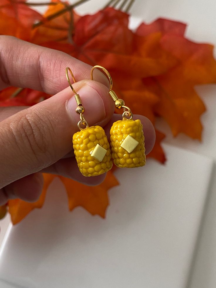 a hand holding two yellow corn on the cob earrings