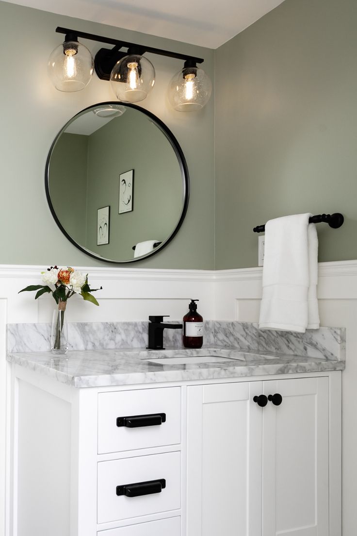 a bathroom vanity with marble counter top and two lights on it's sides, along with a round mirror above the sink