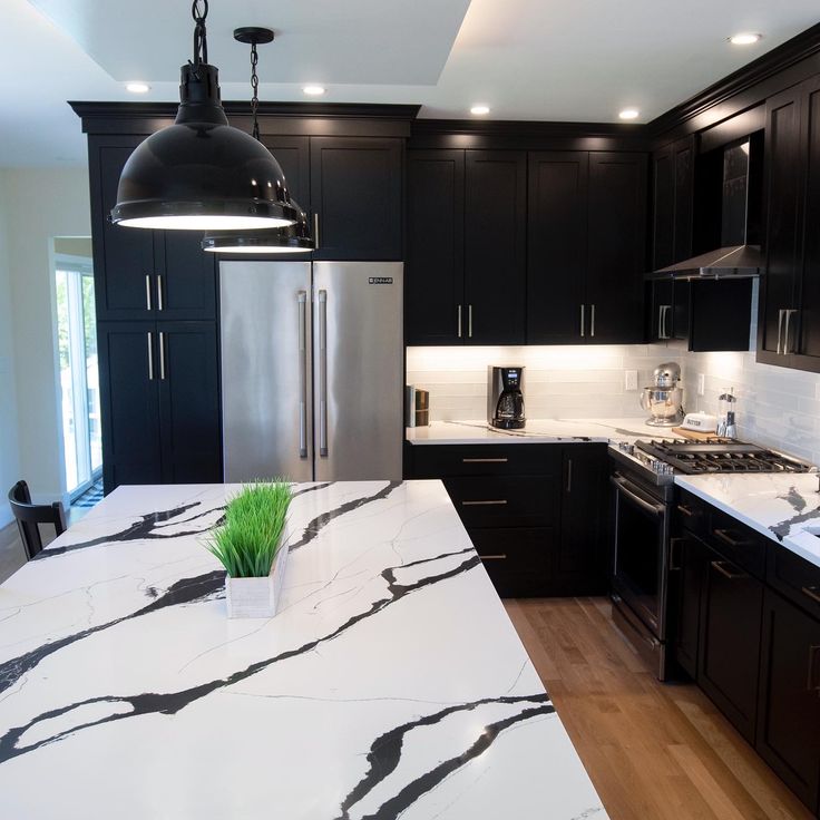 a kitchen with black cabinets and white marble counter tops, an island style sink and stainless steel appliances