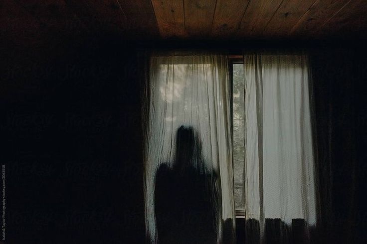 the silhouette of a person standing in front of a window with curtains on either side