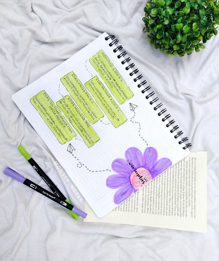 an open notebook sitting on top of a bed next to a pen and flower pot