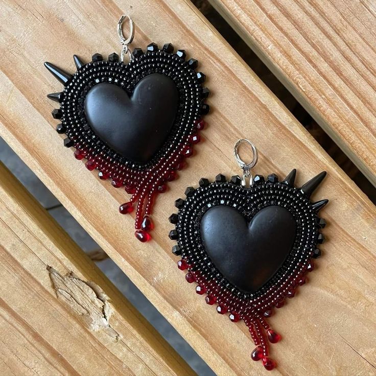 two black heart shaped earrings with red beads and spikes hanging from them on a wooden surface