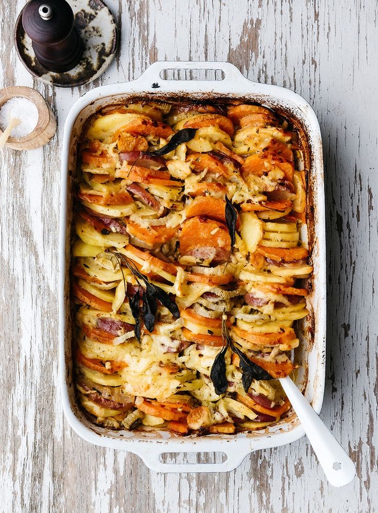 a casserole dish with meat and vegetables in it on a white wooden table