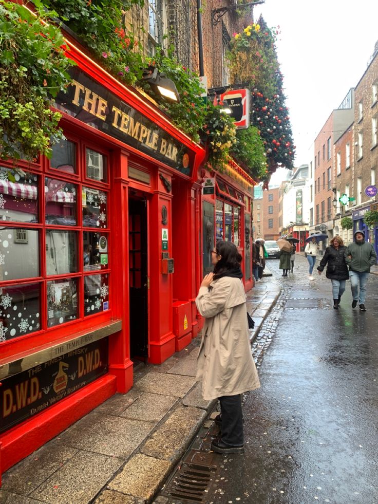 a woman walking down the street in front of a red phone booth on a rainy day