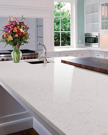 a kitchen with white counter tops and wooden cabinets, flowers in vase on the island