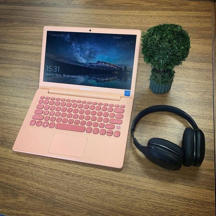 an open laptop computer sitting on top of a wooden desk next to headphones and a potted plant