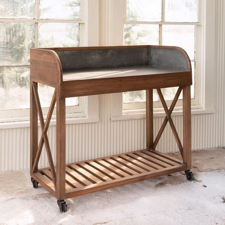 a wooden table with a black leather top on wheels in front of a large window