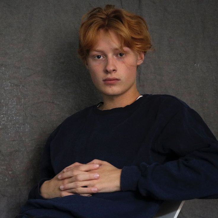 a young man with red hair sitting in a chair and holding his hands on his chest