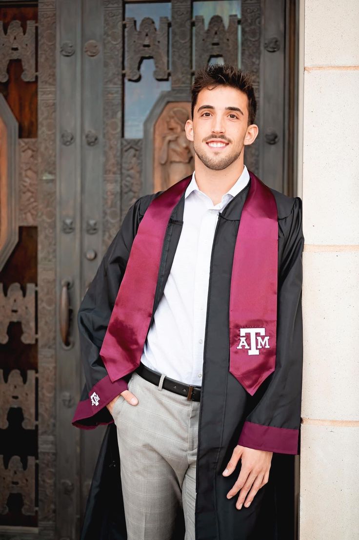 a man wearing a graduation robe and tie standing in front of a door with his hands on his hips