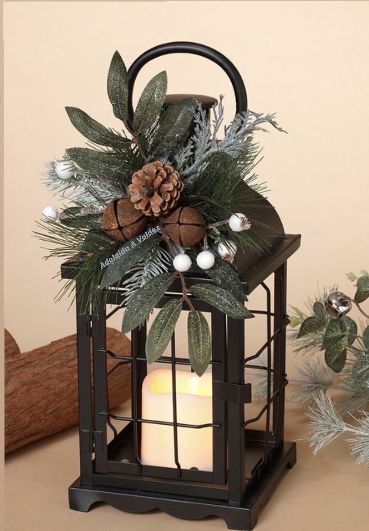 a candle is lit in front of a lantern with greenery and pine cones on it