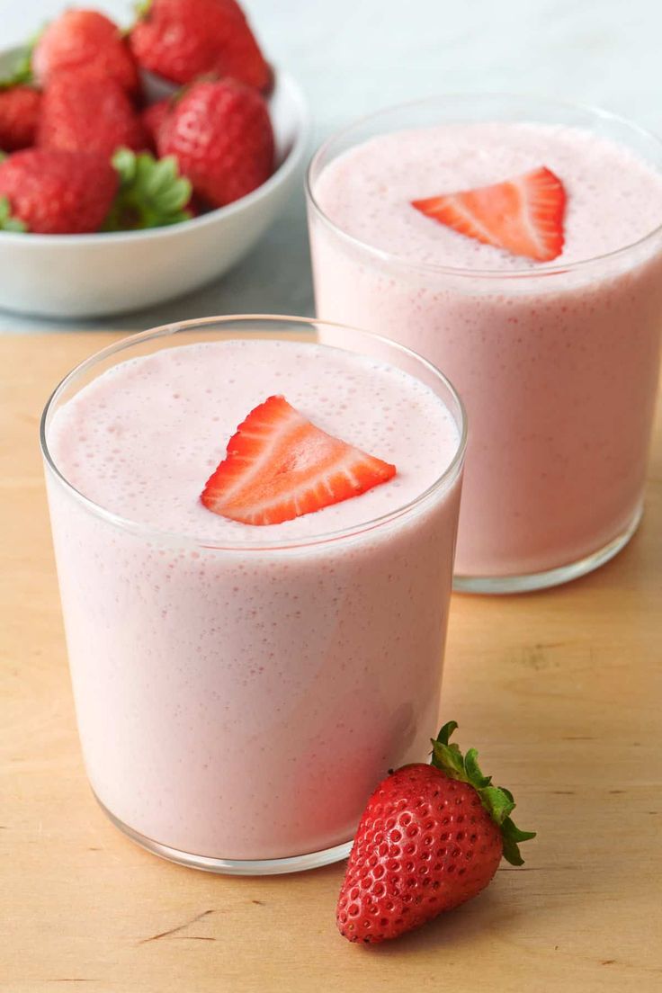 two glasses filled with strawberry smoothie next to a bowl of strawberries