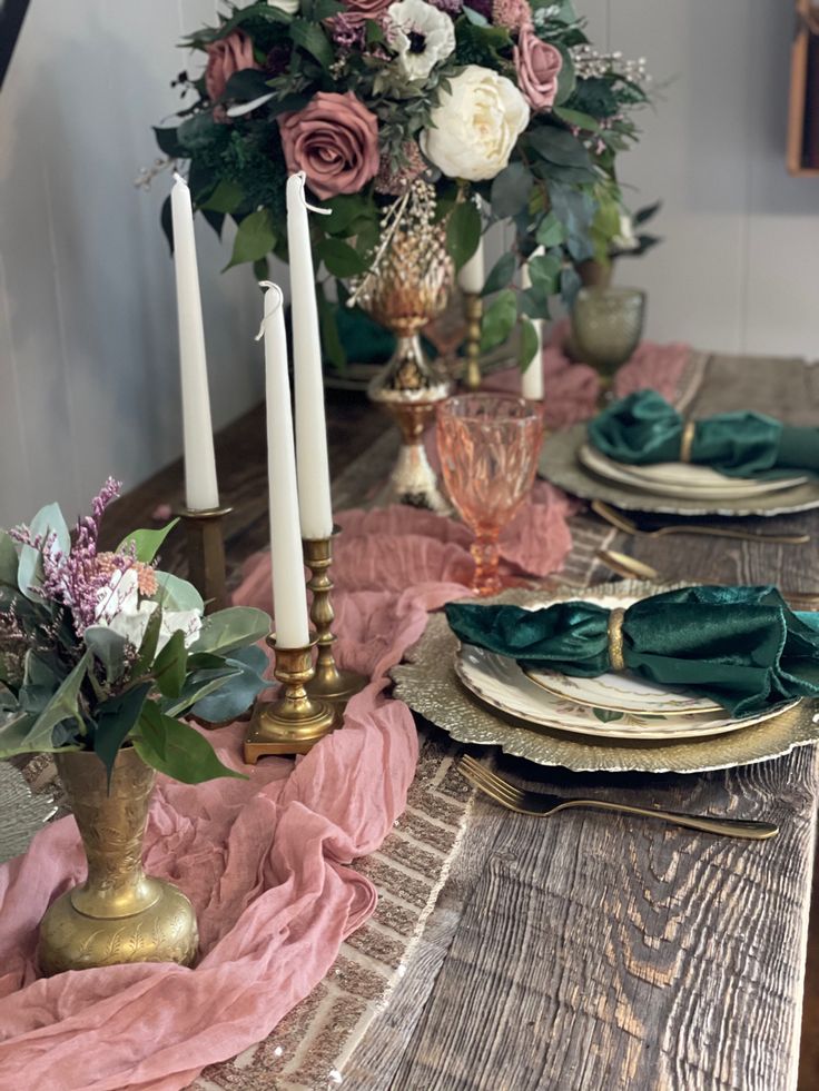 the table is set with pink and green napkins, gold plates, candles, and flowers