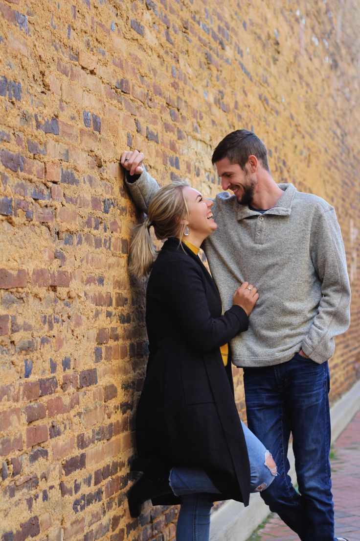 a man and woman leaning against a brick wall