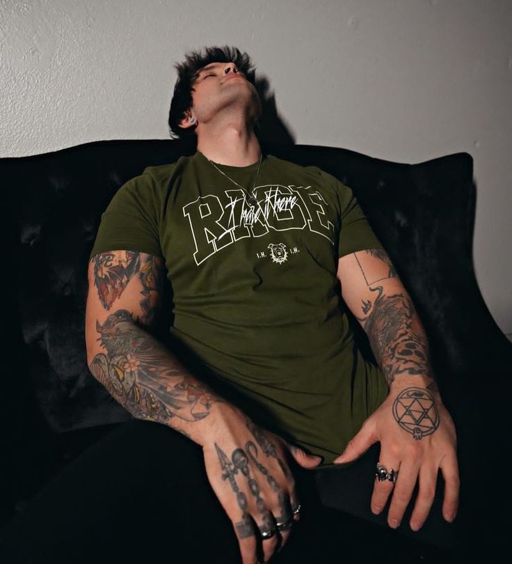 a man with tattoos on his arms and chest sitting on a couch looking up at the sky