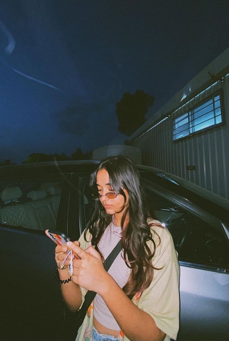 a woman standing next to a car looking at her cell phone