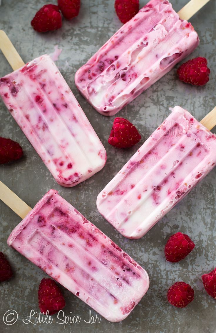 raspberry ice cream popsicles on a baking sheet with fresh raspberries