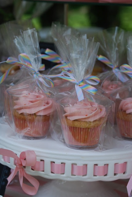 cupcakes with pink frosting and bows are on display in plastic wrappers