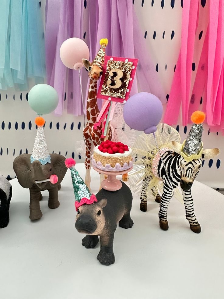 a table topped with figurines and balloons next to zebra, giraffe, elephant cake