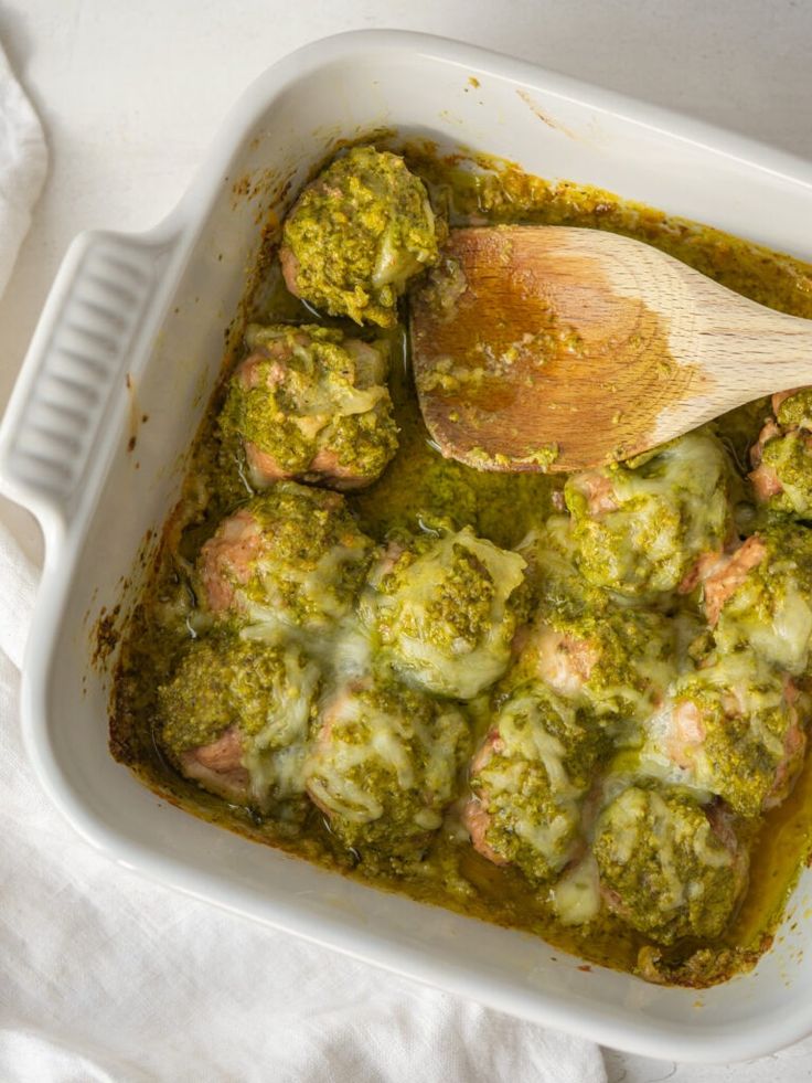 a casserole dish with broccoli covered in sauce and a wooden spoon