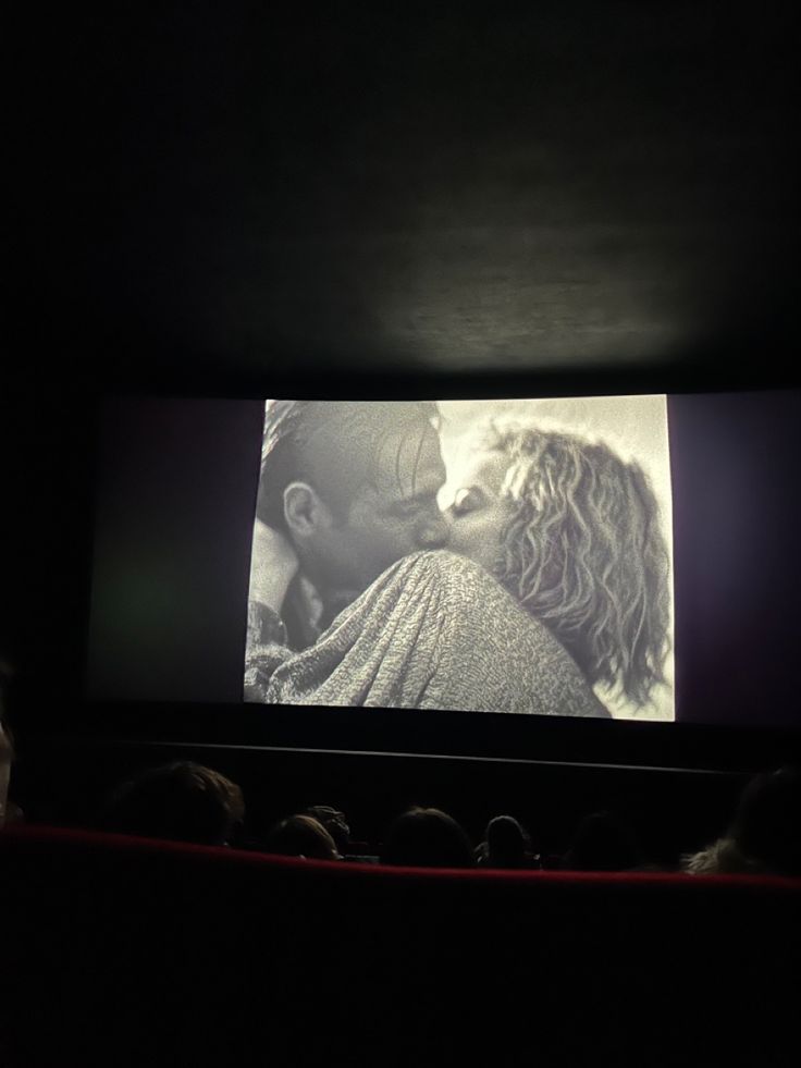 a movie screen with two people kissing in the dark, while one person is watching