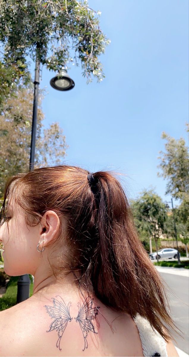 a woman with a tattoo on her back standing in front of a street light and trees