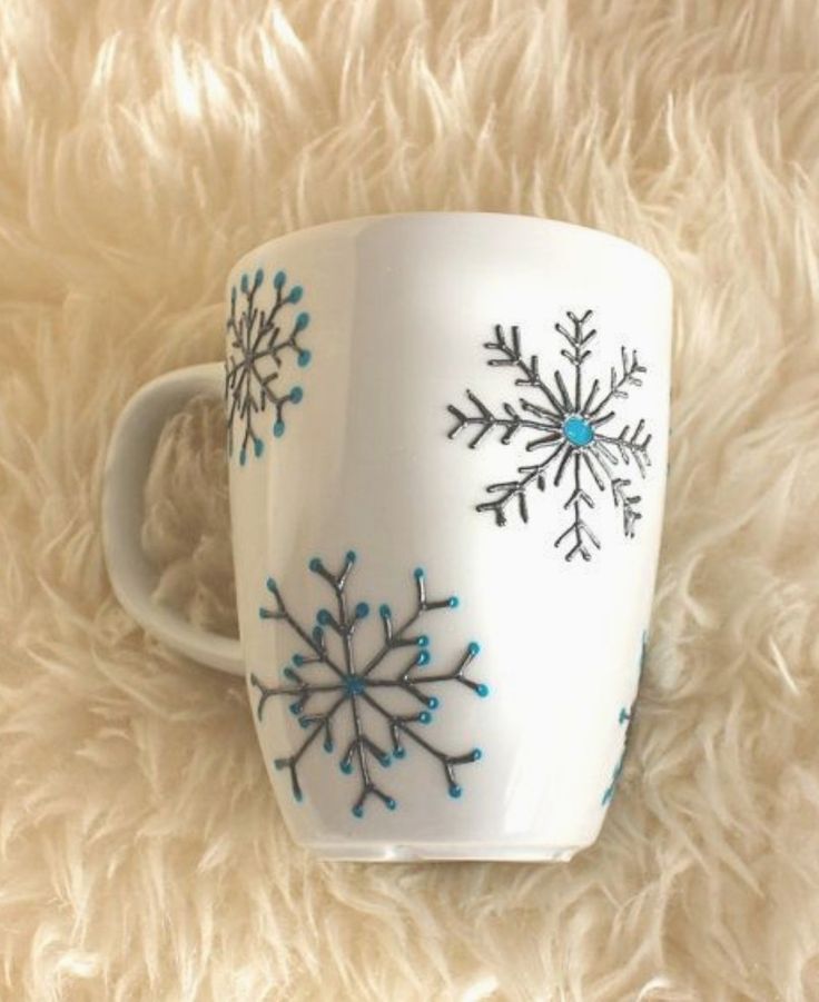 a white coffee cup with blue snowflakes on it sitting on a fluffy surface