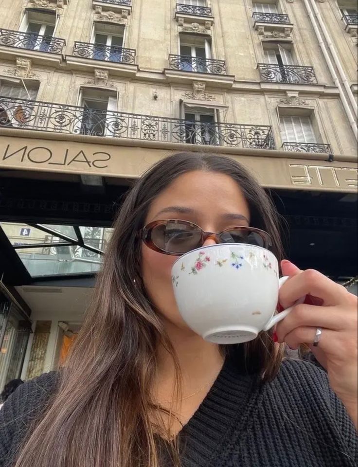 a woman drinking from a coffee cup in front of a tall building