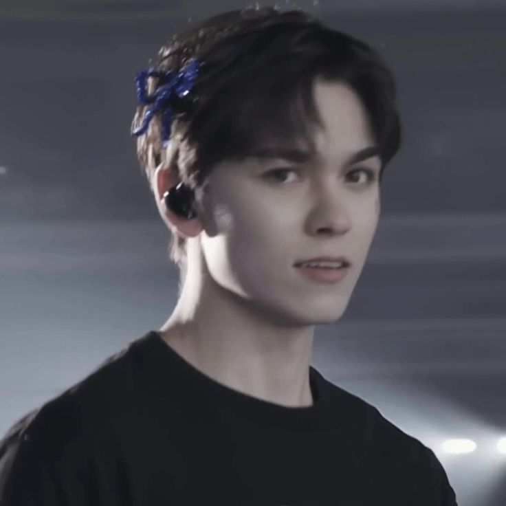 a young man wearing a black t - shirt with a blue bow in his hair