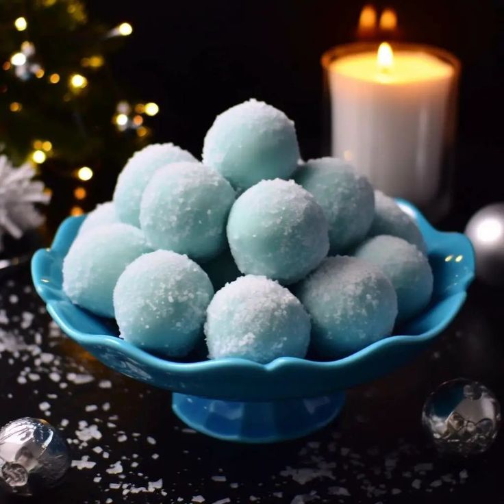 a blue bowl filled with snowballs next to a lit candle