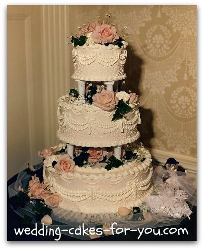 a three tiered wedding cake with pink flowers on the top and bottom, sitting on a table in front of a wall