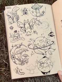 an open book with drawings on it laying in the grass next to someone's hand