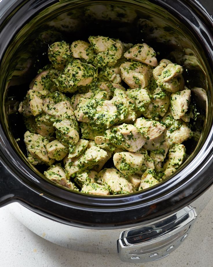 a crock pot filled with broccoli and chicken in pesto cheese sauce