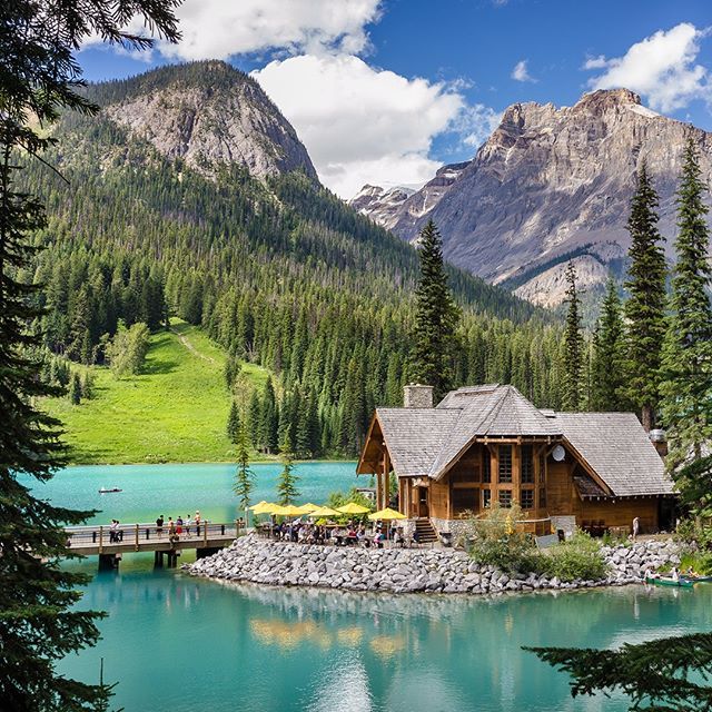 a lake surrounded by trees and mountains with a house on the shore in the foreground