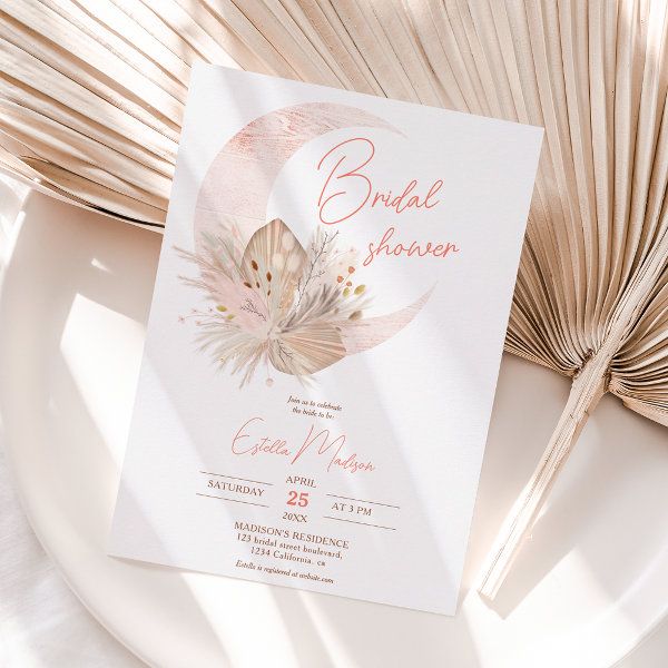 a white and pink wedding card on top of a plate with fan in the background