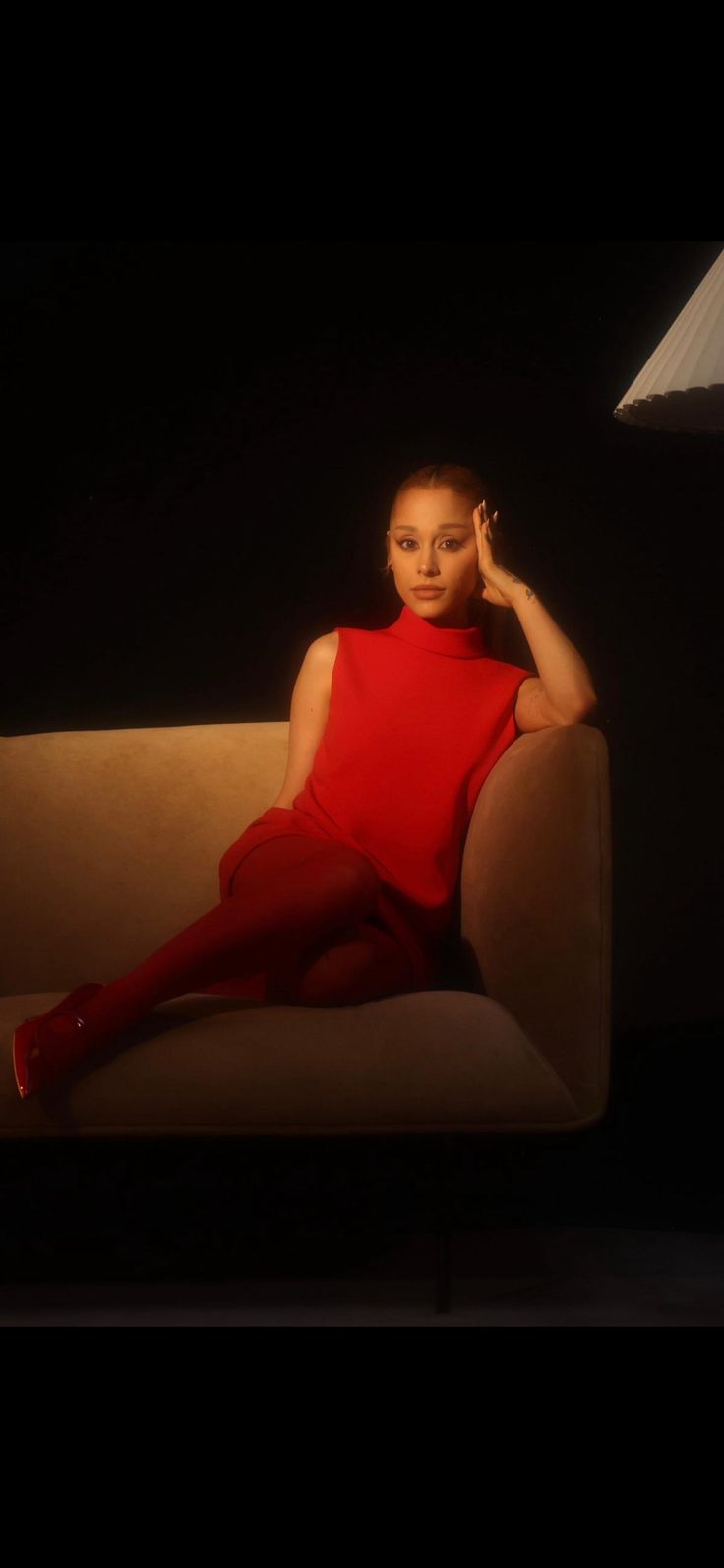 a woman in a red dress is sitting on a couch with her hands behind her head