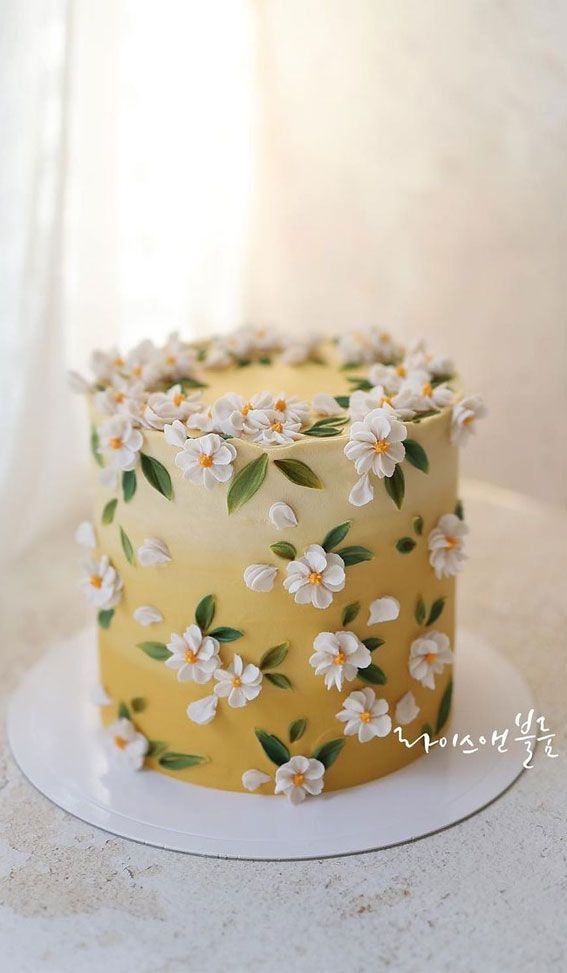 a yellow and white cake with flowers on the frosting is sitting on a plate