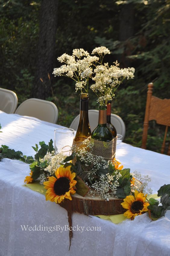 two wine bottles are sitting on a table with sunflowers and baby's breath