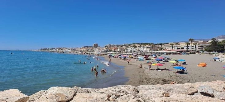 many people are on the beach with umbrellas and in the water there is a blue sky