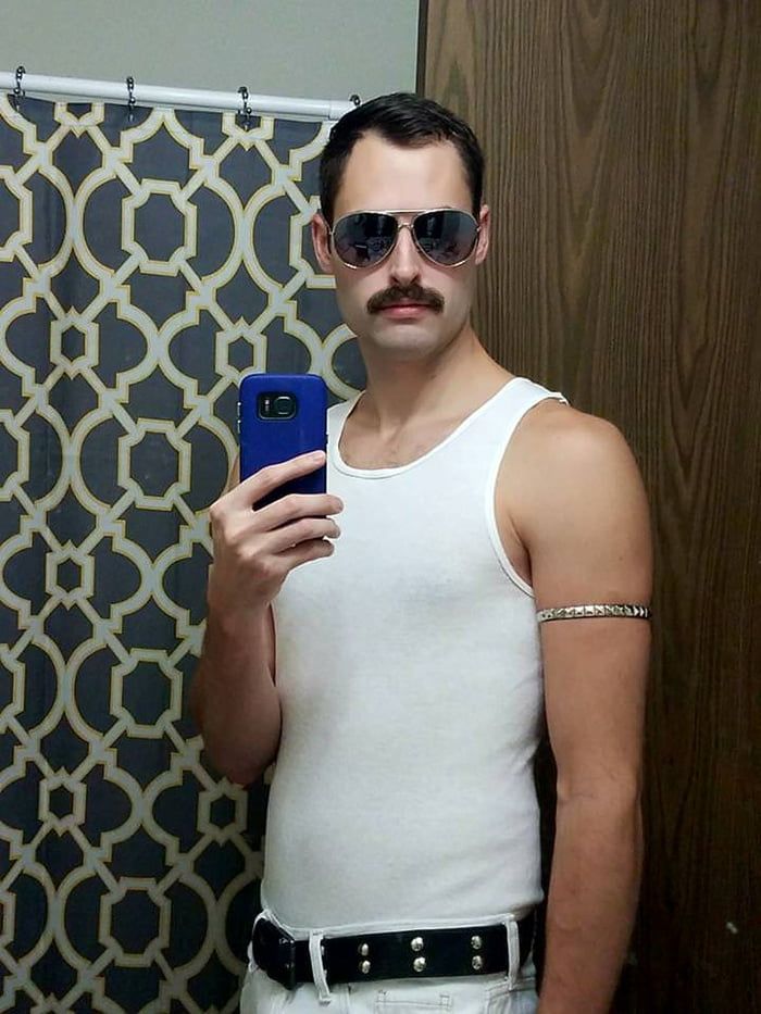 a man in white tank top and sunglasses taking a selfie with his cell phone