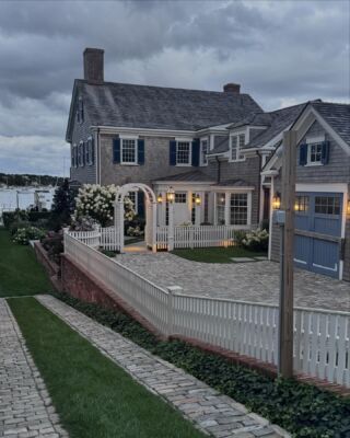 a large house sitting next to a body of water with a white picket fence in front of it