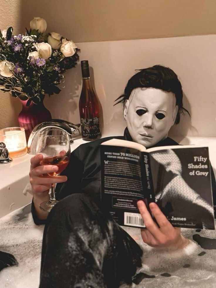 a person wearing a mask is reading a book in the bathtub with a dog