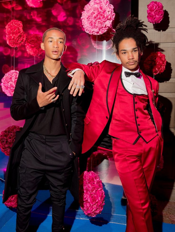 two men dressed in red and black standing next to each other with pink flowers behind them