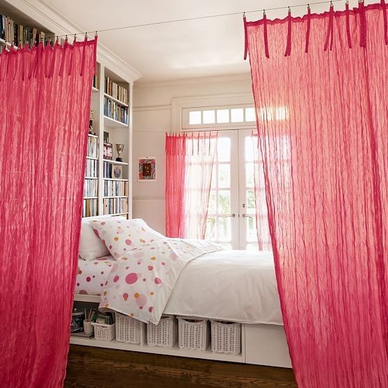 a bedroom with red sheer curtains hanging from the ceiling and a bed in front of a window